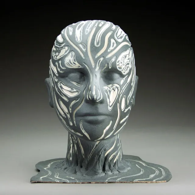 Front view of a ceramic head and neck in matte charcoal gray with closed eyes, inlaid all over with flowing white lines and pools like marbled stone. The pattern continues down the neck and spreads across a flat base that ripples out like spilled liquid.