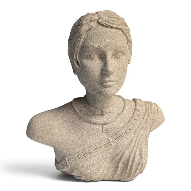 A bust of a woman with short swept-back hair and a calm, direct gaze, finished in a speckled stone texture. She wears a Greek key pendant on a choker and a draped garment across one shoulder, edged with a Greek key border.